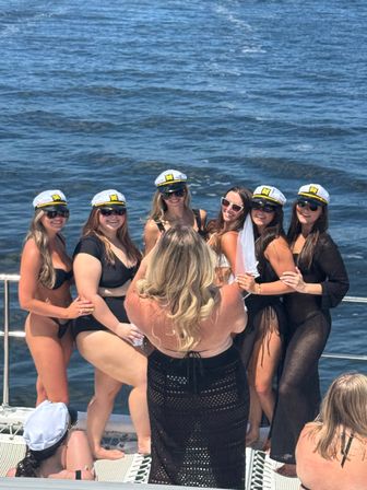 Bachelorette party on a boat: women in bikinis and captain hats, one wearing a veil, posing for a group photo on a sunny ocean cruise