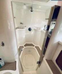 Compact white marine shower stall with glass door, overhead showerhead, built-in corner seats and shelves, and non-slip floor — yacht bathroom interior.