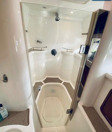 Compact white marine shower stall with glass door, overhead showerhead, built-in corner seats and shelves, and non-slip floor — yacht bathroom interior.