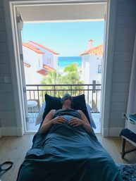 Relaxing spa treatment on a massage table facing a balcony with palm trees, white red-tiled villas and a turquoise ocean view