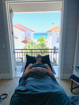 Relaxing spa treatment on a massage table facing a balcony with palm trees, white red-tiled villas and a turquoise ocean view