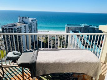 Relaxing massage table on a high-rise balcony overlooking turquoise ocean, white-sand beach and coastal condominium buildings