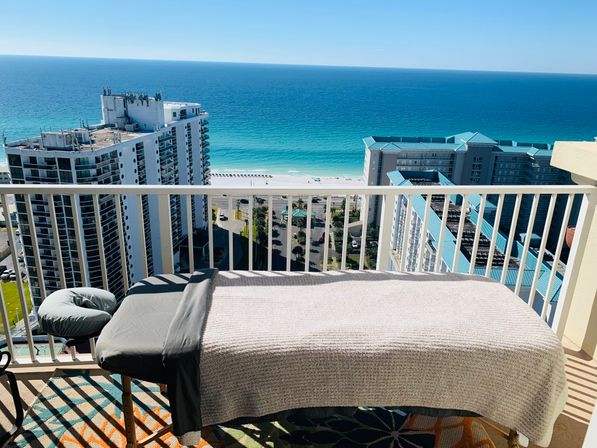 Relaxing massage table on a high-rise balcony overlooking turquoise ocean, white-sand beach and coastal condominium buildings
