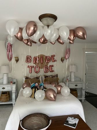 Bridal bedroom celebration with rose gold and white helium balloons floating above a bed and 'BRIDE TO BE' rose-gold foil banner