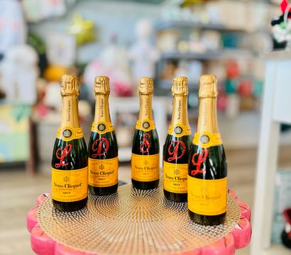 Five Veuve Clicquot champagne bottles arranged on a pink scalloped pedestal — festive display in a colorful boutique gift shop.