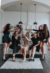 Bachelorette party: bride in a veil and six friends toasting with champagne on a sofa in a bright modern loft-style kitchen with arched wood ceiling and pendant lights
