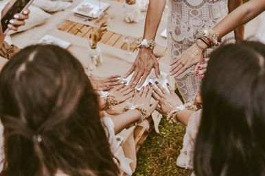 Boho bridal squad placing hands together at an outdoor wedding picnic, lace dress, dried floral wrist corsages and gold “Team Bride” temporary tattoos