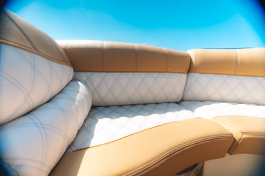 Sunlit tan and white diamond-stitched marine bench seat on a boat under a bright blue sky