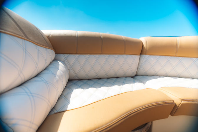 Sunlit tan and white diamond-stitched marine bench seat on a boat under a bright blue sky