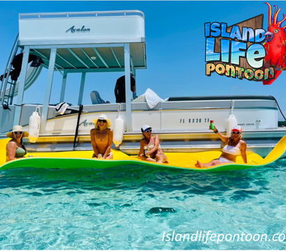 Four people in swimsuits and sun hats lounging on a bright yellow inflatable mat beside a white pontoon boat in crystal-clear turquoise water on a sunny day, holding drinks.