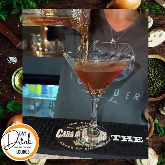 Close-up of a bartender pouring an amber cocktail from a mixing glass into a chilled martini glass on a bar mat in a cozy lounge