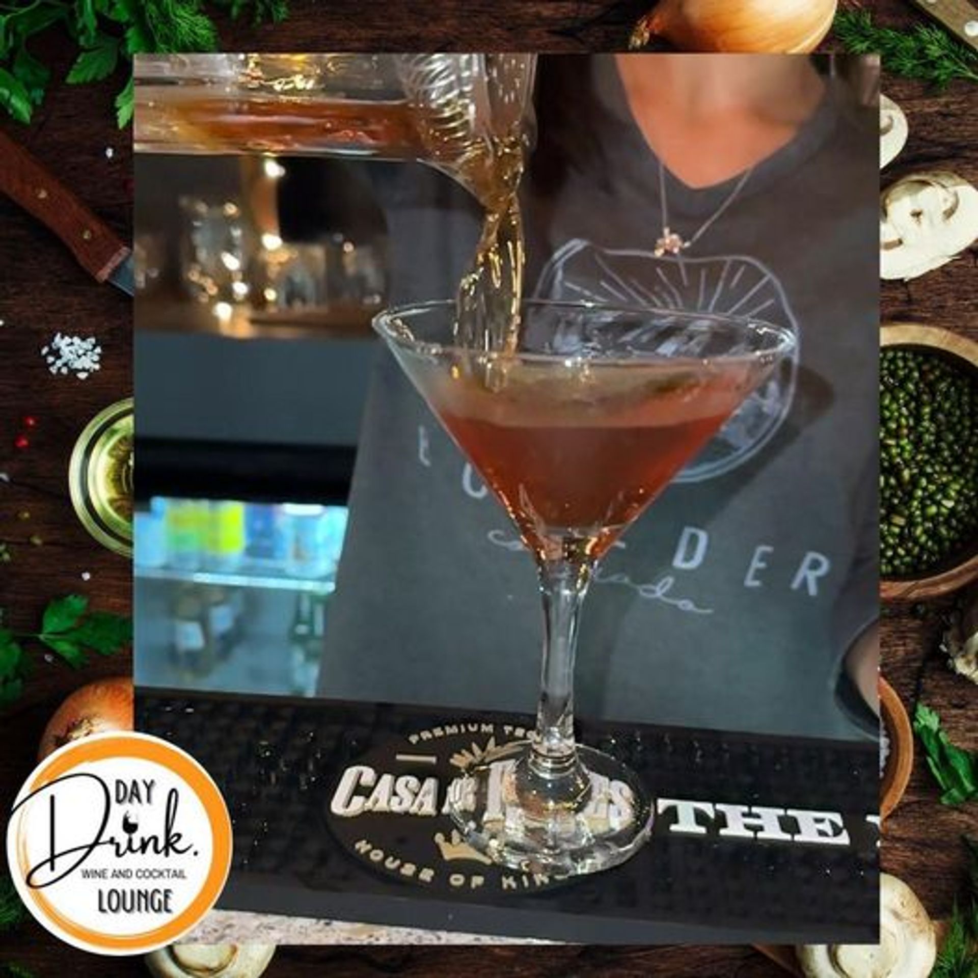 Close-up of a bartender pouring an amber cocktail from a mixing glass into a chilled martini glass on a bar mat in a cozy lounge