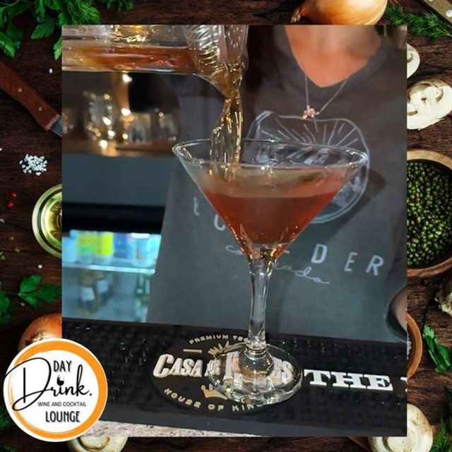 Close-up of a bartender pouring an amber cocktail from a mixing glass into a chilled martini glass on a bar mat in a cozy lounge