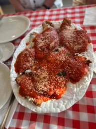 Hearty chicken Parmesan — breaded cutlets smothered in marinara and grated Parmesan on a white platter, served family-style on a red-and-white checkered tablecloth at an Italian restaurant.