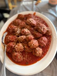 Heaping white platter of Italian meatballs in chunky marinara sauce, sprinkled with grated Parmesan and served with a spoon