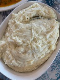Creamy mashed potatoes in a white oval serving dish, speckled with black pepper — a comforting family-style dinner side dish.