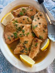 Close-up of Italian-style chicken piccata — pan-seared chicken cutlets in zesty lemon-caper butter sauce, garnished with chopped parsley and lemon wedges on a white plate.
