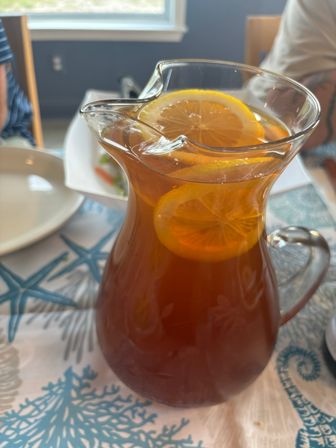 Glass pitcher of iced tea with floating lemon slices on a sea-themed starfish tablecloth at a dining table