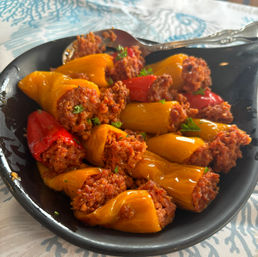 Close-up of roasted red and yellow stuffed mini peppers appetizer—bite-sized sweet peppers filled with savory spiced meat and parsley, served in a black bowl.