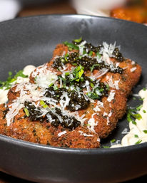 Gourmet crispy breaded cutlet topped with glossy black caviar, shaved Parmesan and fresh chives, served with dollops of aioli in a matte black bowl.