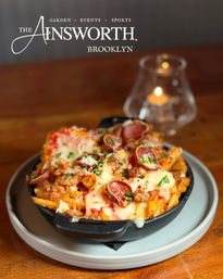 Skillet of loaded fries topped with melted cheese, pepperoni, bacon and chives on a plate at a candlelit Brooklyn restaurant