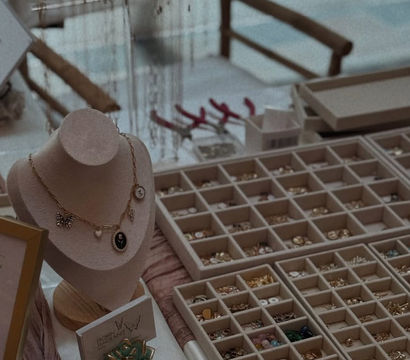 Velvet necklace bust displaying a charm necklace beside organized trays of rings and earrings on a market table, with jewelry tools and a small ceramic succulent.