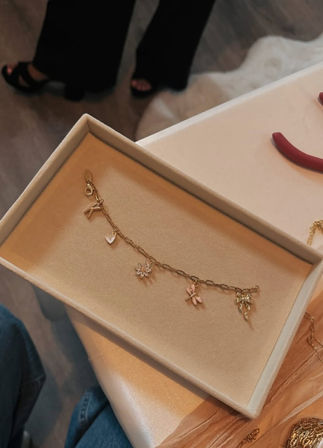 Delicate gold charm bracelet with heart, flower and dragonfly charms nestled in a beige velvet jewelry box on a table, close-up