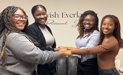 Four smiling women in a casual studio joining fists in a team fist-bump, friendly small-team vibe.