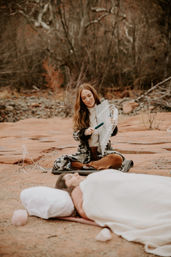 Sound healing on red sandstone: woman in a red-rock desert canyon plays metal chimes with a mallet beside a resting person.