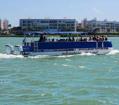 Blue-canopy pontoon tour boat full of passengers cruising turquoise coastal waters past beachfront condominiums under a sunny sky