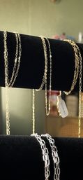 Close-up of shiny gold and silver chain necklaces draped over a black velvet jewelry display, showing mixed link styles and a small hanging tag.