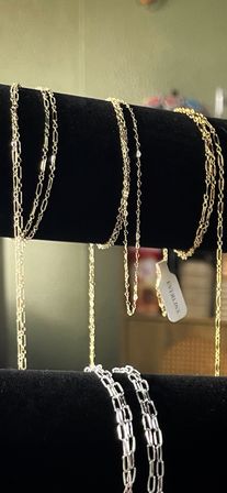 Close-up of shiny gold and silver chain necklaces draped over a black velvet jewelry display, showing mixed link styles and a small hanging tag.