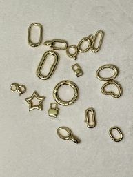 Flat-lay of scattered gold-tone jewelry findings and charms on beige fabric — oval links, round spring ring, lobster clasp, star and heart charms for DIY jewelry and accessories.