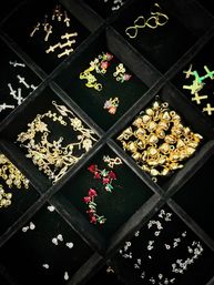 Close-up of a black velvet jewelry organizer filled with sparkling gold and silver charms and findings — heart and cross shapes, red crystal pendants, and rhinestone connectors.