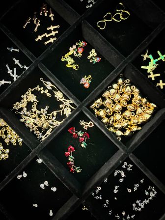 Close-up of a black velvet jewelry organizer filled with sparkling gold and silver charms and findings — heart and cross shapes, red crystal pendants, and rhinestone connectors.