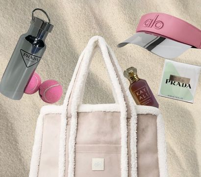Beach-ready plush shearling-trimmed pink tote on sand surrounded by a mirrored water bottle, pink visor, two pink tennis balls, a perfume bottle and a skincare sachet