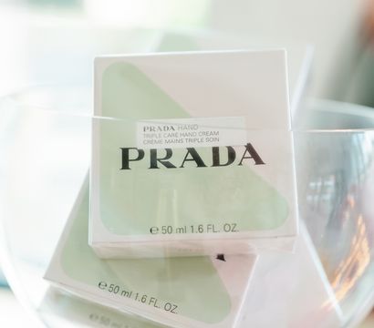 Stacked pastel green-and-white boxed luxury hand creams (50 ml / 1.6 fl oz) displayed in a clear glass bowl on a bright, minimalist countertop.