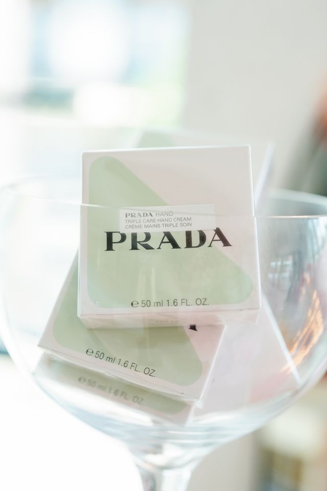 Stacked pastel green-and-white boxed luxury hand creams (50 ml / 1.6 fl oz) displayed in a clear glass bowl on a bright, minimalist countertop.