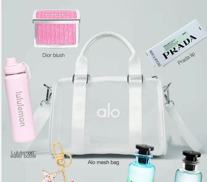 Chic clear white mesh duffel bag styled with a pink blush compact, pale pink water bottle, boxed lip balm, designer keychain and two small perfume bottles on a soft gray background.