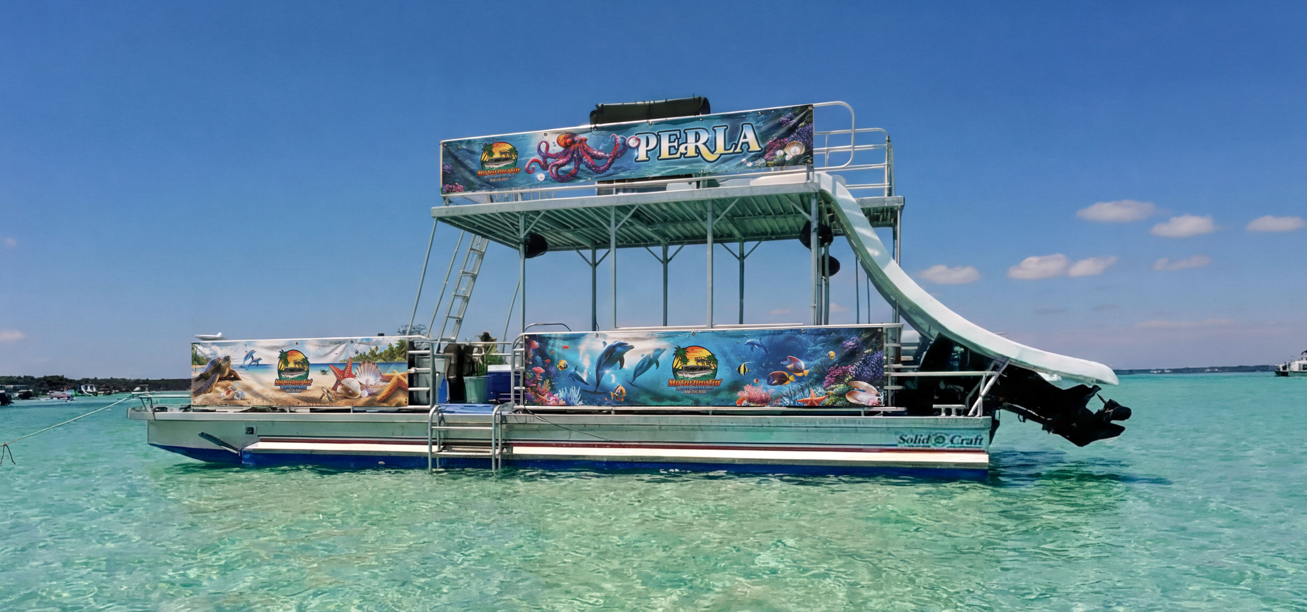 Double-decker pontoon boat with a curved water slide and colorful ocean-themed murals floating in shallow turquoise tropical water under a clear blue sky