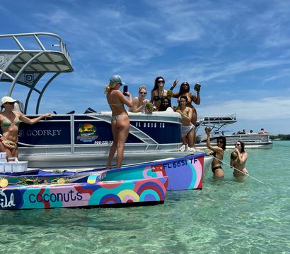 Group of friends on a pontoon and colorful small boat at a tropical sandbar, sunlit clear turquoise shallow water, women in bikinis holding coconuts under a bright blue sky.