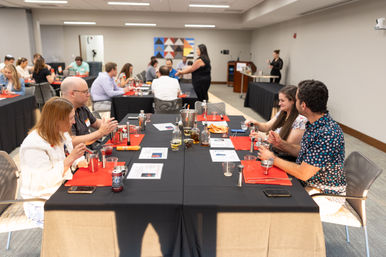 Adults at a mixology workshop in a conference room, seated at tables with shakers, jiggers, bottles and recipe sheets