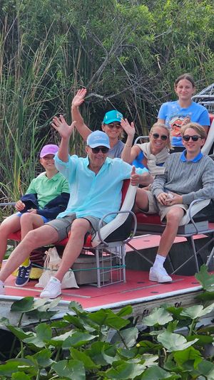 Group of people waving from a red-deck airboat cruising through lily pad–filled wetlands with tall reeds — Florida Everglades airboat tour vibe