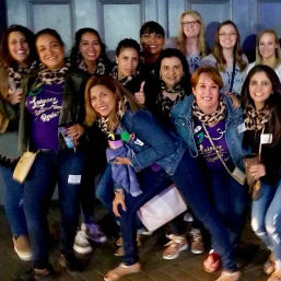 Group of smiling women in matching leopard-print scarves and purple tops posing on a downtown sidewalk at night for a girls’ night out