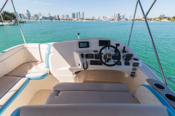 Sunlit yacht helm with quilted leather seating, steering wheel and navigation screens overlooking turquoise bay and the Miami skyline