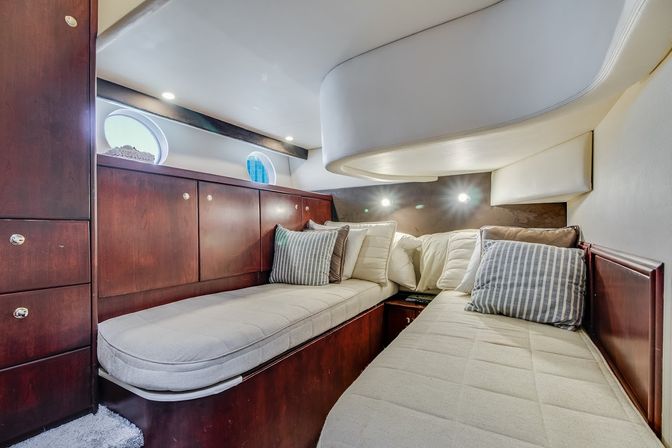 Cozy yacht cabin with twin berths, rich wood cabinetry, round portholes, striped throw pillows and warm recessed lighting