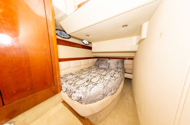 Cozy yacht cabin interior with a snug double bed dressed in gray damask bedding, cream padded walls, glossy wood trim and two small round portholes.