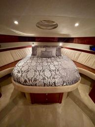 Luxury yacht forward stateroom with rounded queen bed dressed in gray damask bedding, plush beige leather wraparound seating, warm wood trim, overhead hatch and recessed lighting