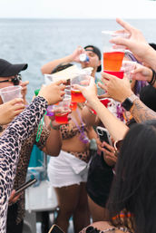 Group toasting with colorful plastic cups aboard a party boat on the ocean — lively summer celebration at sea
