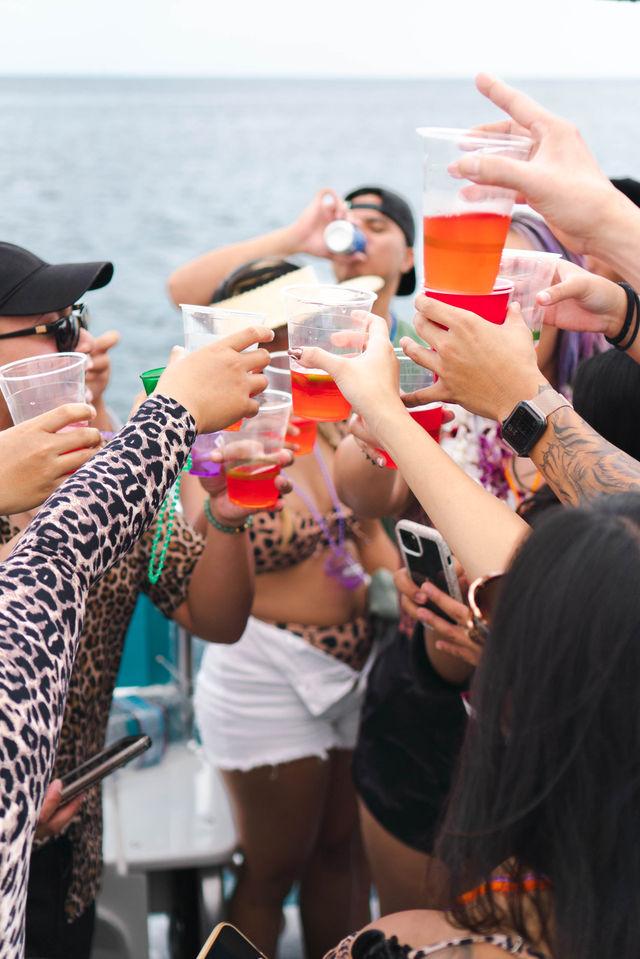 Group toasting with colorful plastic cups aboard a party boat on the ocean — lively summer celebration at sea